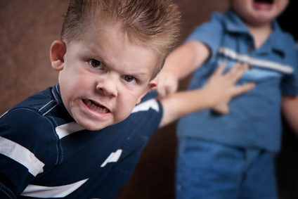 Angry little boy glaring at the camera, fighting with his brother who is screaming